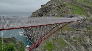 The red metal bridge at Tintagel Castle where it is though King Arthur lived. Slow motion footage of the bridge and surrounding landscape, cliffs and sea on a misty summer day