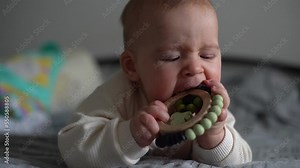 baby chewing teether toy. Infant growing first tooth. Boy biting toy on parents bed. Pretty six-month old baby boy. Realistic toddler home portrait