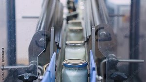 Glass containers jars filled with milk move along a conveyor at a dairy factory. Food industry, jars with baby food, kefir, yogurt in the dairy products bottling shop.