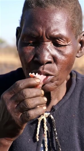 Elderly Hadzabe Woman Enjoying Traditional Fire-Cooked Meal@viralmunchies-ai