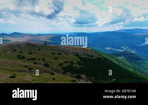 Wide alpine landscape with rolling peaks. Green pastures cover the slopes under a cloudy sky.