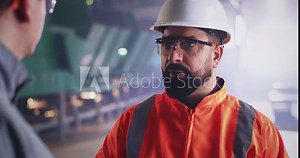 Bearded inspector speaking with worker on factory