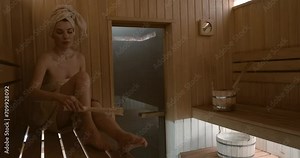 Woman relaxing and sweating in hot sauna wrapped in towel. Girl In Spa. Interior of Finnish sauna. Classic wooden bathhouse with hot steam. Russian sauna. Relax in hot bathhouse. Classic sauna