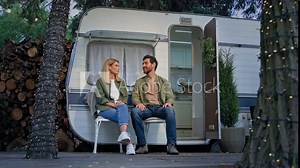 Married couple husband and wife Caucasian family sitting in camping campsite outdoors near van talking suddenly little girl daughter open window in trailer cuddling mom hugging parents vacation trip
