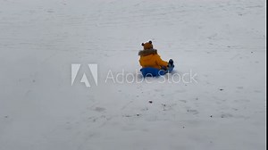 child little boy sledding down a hill onto a frozen pond in winter park