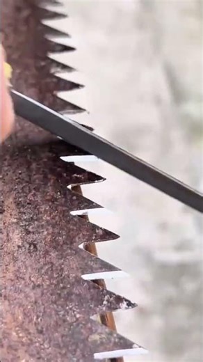 Sharpening the teeth of a rusty manual saw using a small metal file to restore its cutting ability