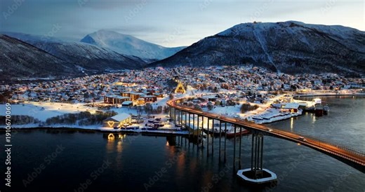 Drone view of Tromsø, Northern Norway in winter, with bridge lights, snowy town streets and fjord water at blue hour, creating a festive Christmas atmosphere