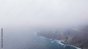 A drone captures the foggy aerial view of Californias Big Sur coast along Highway 1, displaying the areas natural beauty in a rugged landscape with stunning cliffs and the vast ocean