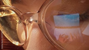Close-up shot of woman eyes in glasses reflecting a working computer blue screen. Focused on work woman looking at laptop. Macro female eyes. Person watches hypnotizing index finger.