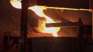 A furnace in which metal is melted. Sparks and smoke from the fire. metallurgical industry.Pouring bright hot liquid steel or metal from ladle in blast furnace foundry metallurgical factory.