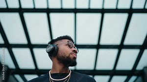 Young satisfied Black man dances freely under an urban grid, his headphones gateway to rhythm of the city,embracing beat in blissful movement. African American male enjoy music playlist with earphones