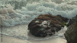 Captivating slow motion footage of waves gently rolling over a grass-covered ocean rock, highlighting the serene interaction between sea and land.