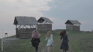 three girls in dresses running on the grass, summer houses, village Stock Video