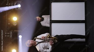 DJ Playing Music in Nightclub. Saxophonist man with saxophone standing in nightclub playing sax, dancing, performing on concert musician stage with DJ man. Party, music festival concept.