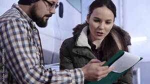 A young girl, a customer of a service station, signs documents with a car mechanic about accepting a repaired car.