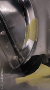 Vertical slow motion footage of a potato slicer slicing potato into chips, with blur background