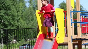 Little cute girl сlimbs and slides on children playground at summer day
