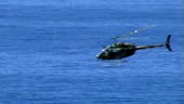 Am army heicopter moves quickly over the ocean past a headland.