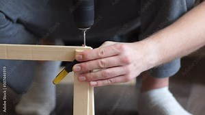 Handyman, young man uses a drill to join pieces of wood, simple home woodworking