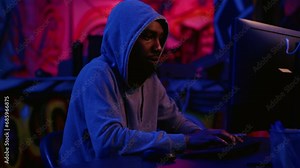 Hacker in secret dark room writing lines of code on computer, developing virus that get past security systems. Evil developer uses PC in hidden bunker, running hacking script