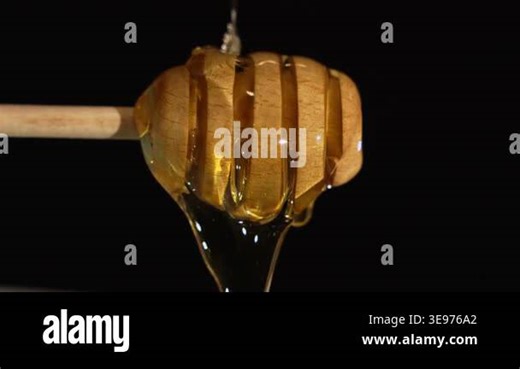 Golden honey drips smoothly from a wooden dipper against a black background, creating a visual flow that enhances its natural sweetness and richness. The honey glistens in the light Stock Video Footage - Alamy