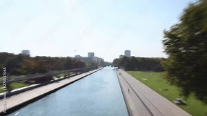 Parc de la villette in Paris with the Geode at Cite des Sciences. Big park with people lying on grass, tanning, water and buildings background with beautiful blue sky during summer. Dezoom effect.