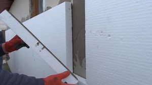 Construction worker installing styrofoam insulation sheets on house facade wall for thermal protection