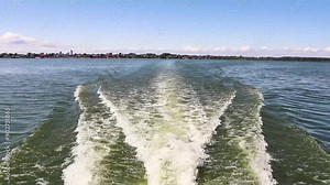 Back view boat cruises along a river, leaving a foamy trail in its wake. Water entertainment, transportation by water concept.
