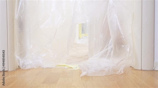 A black and tan dachshund wearing an orange safety vest and helmet runs out of a room covered in plastic sheeting.
