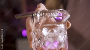 Bartender's hand mixologist pouring cocktail using strainer to make classic Negroni cocktail in a beautiful modern trendy bar. Purple light.