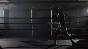 Kickbox fighter shadow boxing in the ring. The athlete fights with his shadow. Young boxer in training throwing a punch with bandages on his fists as he works out in the ring