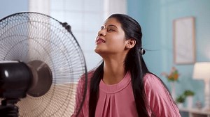 Indian woman using electric fan during hot summer day by sitting in front at home - concept of hot temperature, summertime and relaxation.