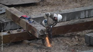 Angular saw grinding through construction piles at construction site. Sharp circular cutter blade spins before grinding into gray cement pile. Engineer in white helmet cutting into large concrete pipe