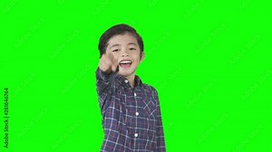 Little boy looks mocking someone by laughing and pointing at the camera in the studio. Shot in 4k resolution with green screen background