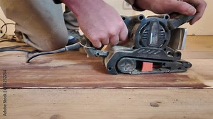 Carpenter hands hold a sanding machine. A woodworker carefully sands a wooden floor using a sanding machine. Home renovation. Sanding with electric sander polisher. Horizontal video.