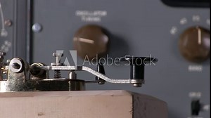 Extreme close-up of finger pressing telegraph key to send morse code radio transmission with vintage electronic hardware engineering military lab test equipment device in the background