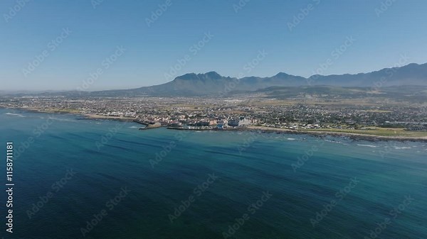 Aerial wide shot of Gordons Bay with coastline and sandy beach in suburb of Cape Town. Beautiful landscape and mountains in distance. Sunny day in South Africa.