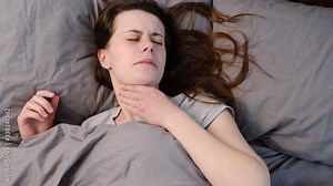Top view of tired unhealthy sick young woman lying down on bed suffering from throat sore, touching neck, having painful feeling, unwell sad female suffering from angina or tonsillitis