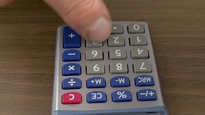 Closeup push-in shot of a finger tapping a calculator on an office desk.