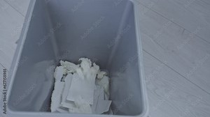 Disposing of crumpled napkins in trash bin with used paper on wooden floor. Waste in container. Dry wipes disposal in grey basket concept