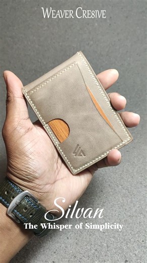 Introducing “Silvan” — The Whisper of Simplicity Model No.: WC-C40 Size: 7.3 cm × 10.5 cm In a world of noise and clutter, Silvan was born to be quiet. A silhouette so slim it disappears in your pocket yet within, it carries intention. Every stitch whispers of care. Every curve, a promise of balance. Crafted in a soft ash-taupe leather, the wallet’s design is clean but curious a secret pull-tab for quick access, an ID window framed like a portrait, and a grain of warm wood peeking through like e