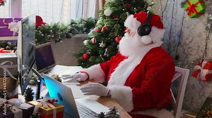 Modern Santa Claus wishes children merry Christmas remote virtual connection sits at desk with laptops and computer, Happy New Year holidays, in home office decorated with Xmas tree and garlands. Stock Video