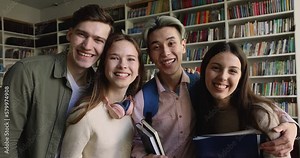 Diverse cheerful high school girls and guys showing thumbs up at camera, making like signs, hugging, enjoying unity feelings, friendship, teamwork, education activities, posing in library