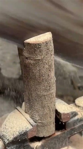 shaping a rectangular wooden block against a rotating industrial sanding belt machine in a workshop