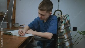 Online education, distant learning concept. Schoolboy sits at computer takes notes in copybook during distance home education.