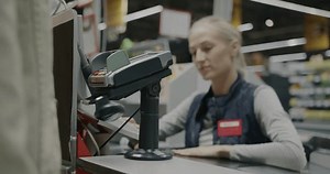 Close-up of male hand making payment with credit card at cashiers desk while saleswoman talking to customer. Retail and finance concept.