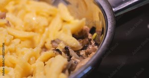 A close-up view captures the cooking process of Spatzle, a traditional Central European egg noodle dish, commonly paired with meat and sauce, now enhanced with the addition of mushrooms