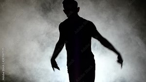 Silhouette of a talented young break dancer. Hip hop street dance on a stage in front of the spotlight. Slow motion. Close up.