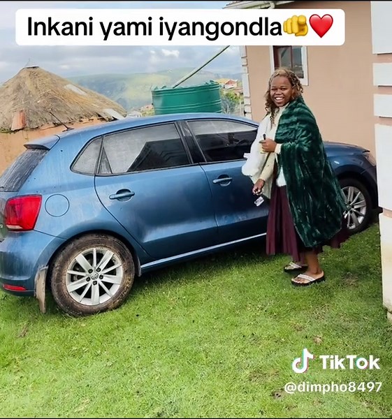 Woman in Green Robe Opens Blue Sedan in Rural Setting