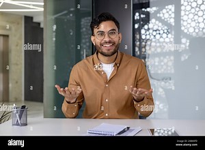Smiling young Indian man sitting in the office at the desk and talking on a video call, making an online recording, conducting training remotely Stock Photo - Alamy